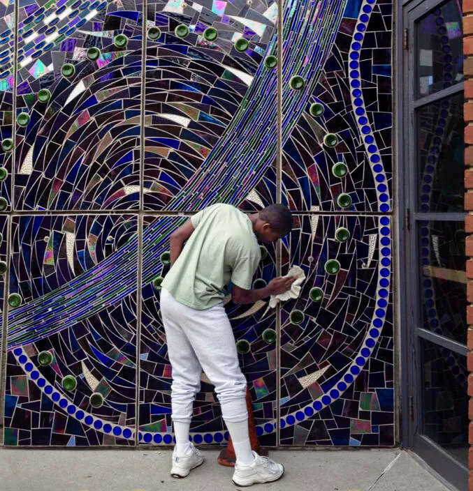 A young man polishing the installed Aurora Borealis mosaic, a swirl of blue and violet glass and bottle bottoms