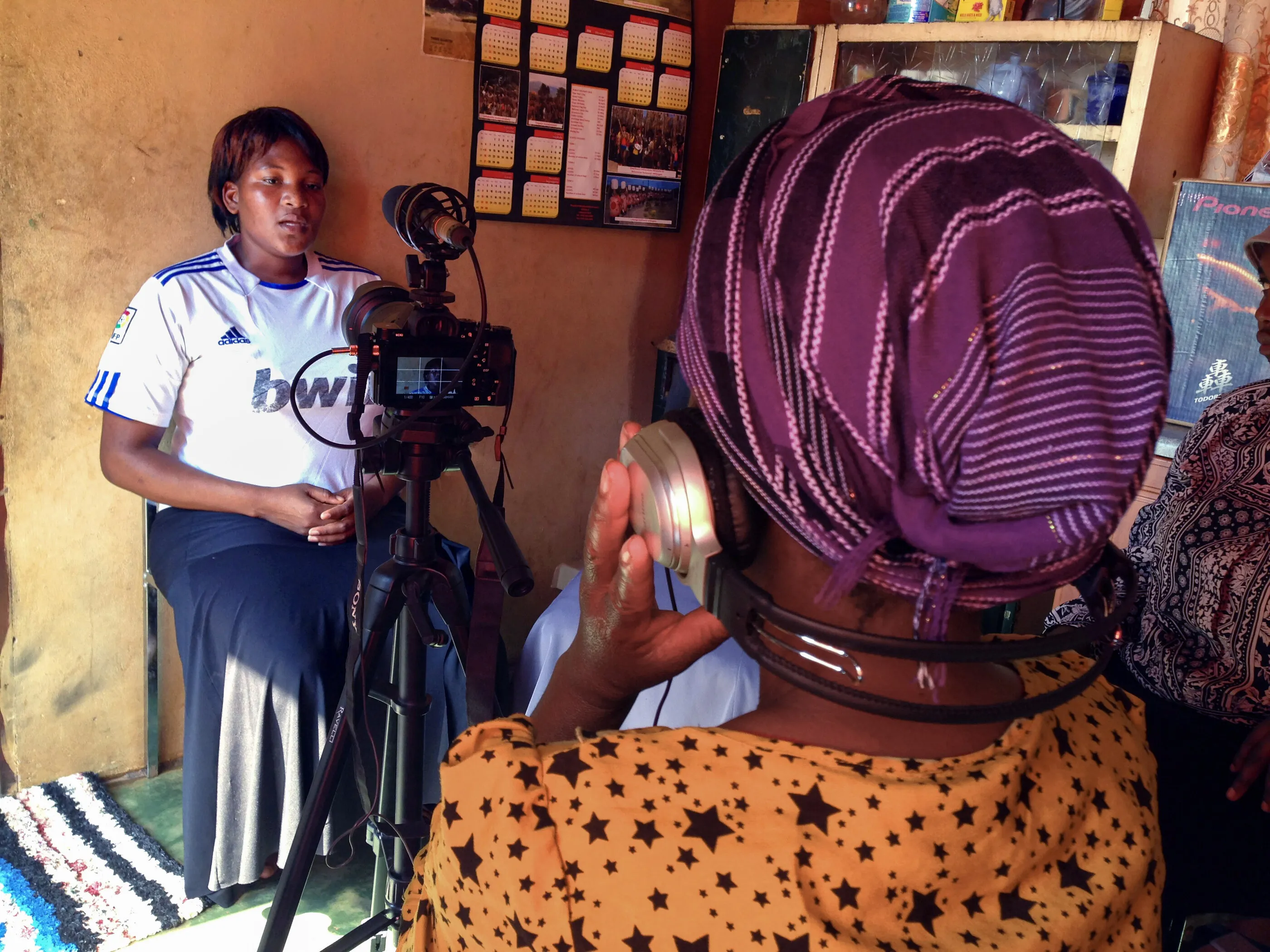 Women filming an interview indoors in Eswatini, one behind the camera on a tripod and one being interviewed