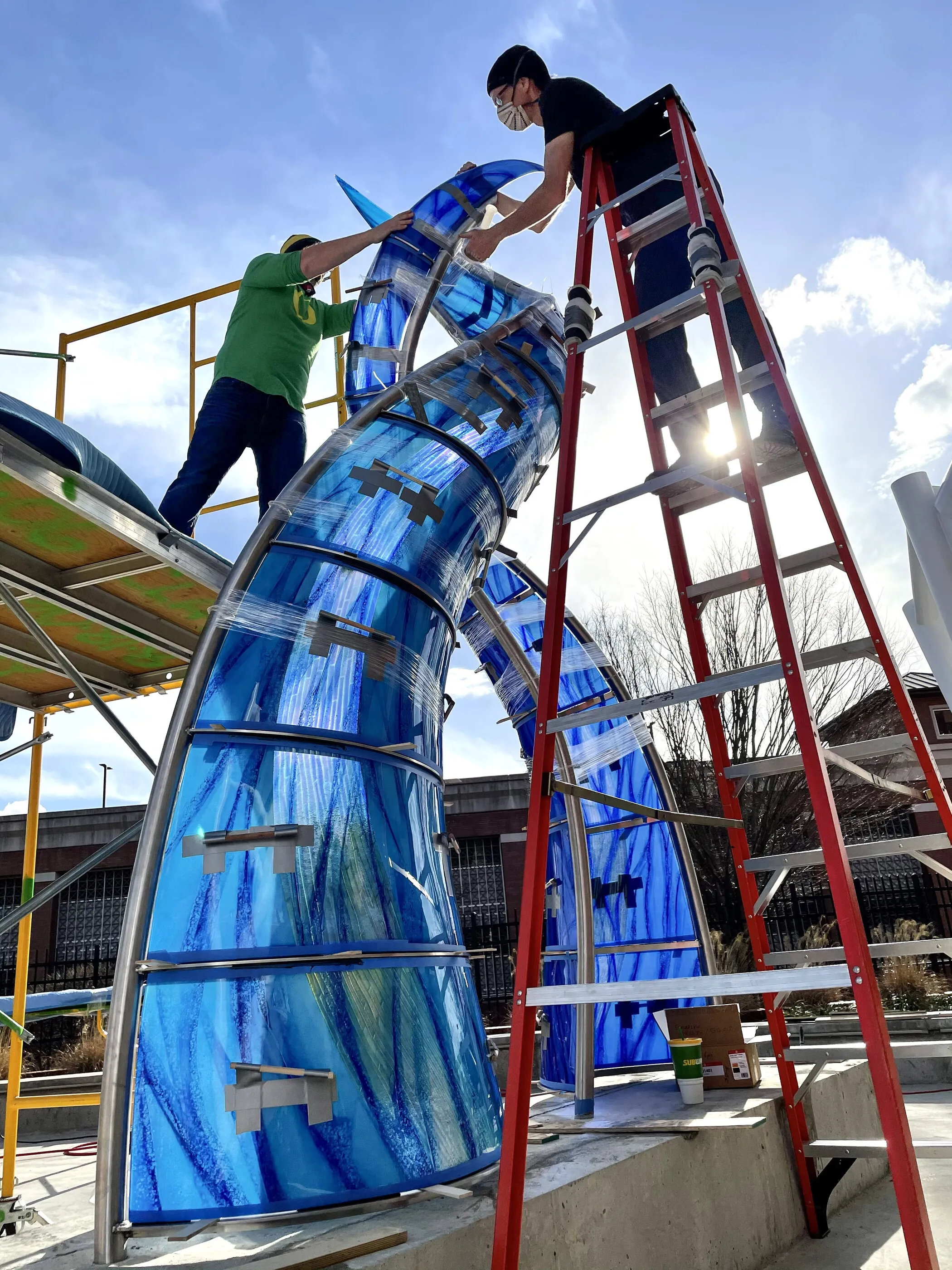 Two people on ladders fitting the last glass panels onto River Waltz on site