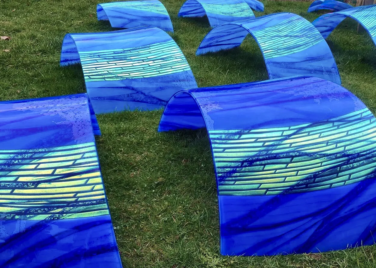 Rows of slumped blue and green glass panels for River Waltz, curved and laid out on the grass