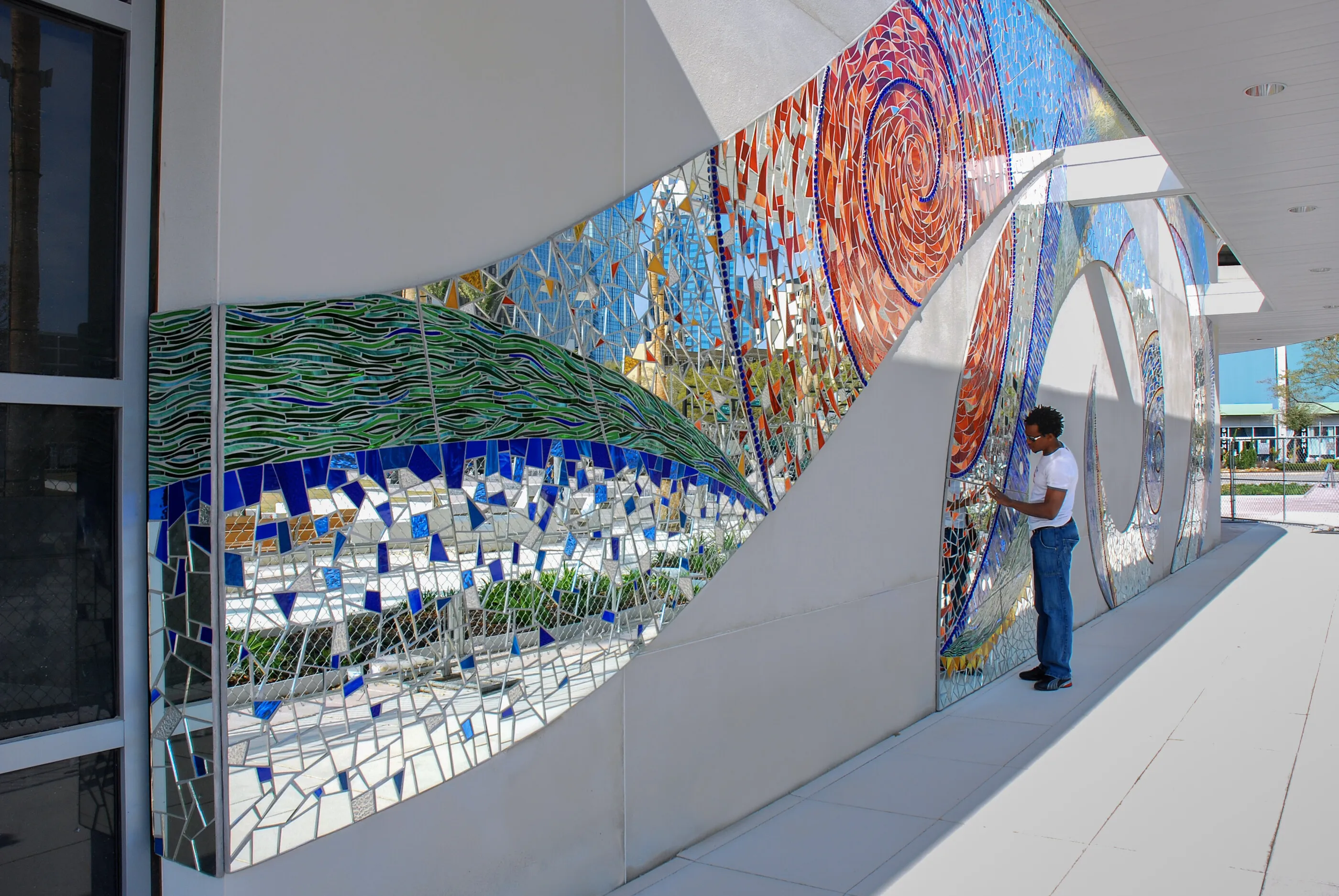 Spiral Fantasia, a long glass and mirror mosaic of blue, green and red spirals along the exterior wall of the Glazer Children's Museum, with a person standing beside it for scale